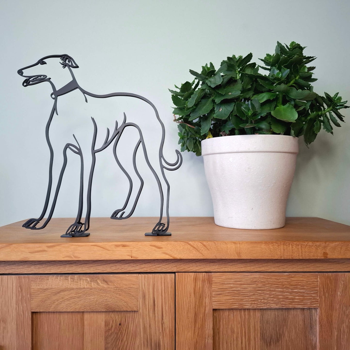 greyhound dog sculpture on a wooden surface next to a plant