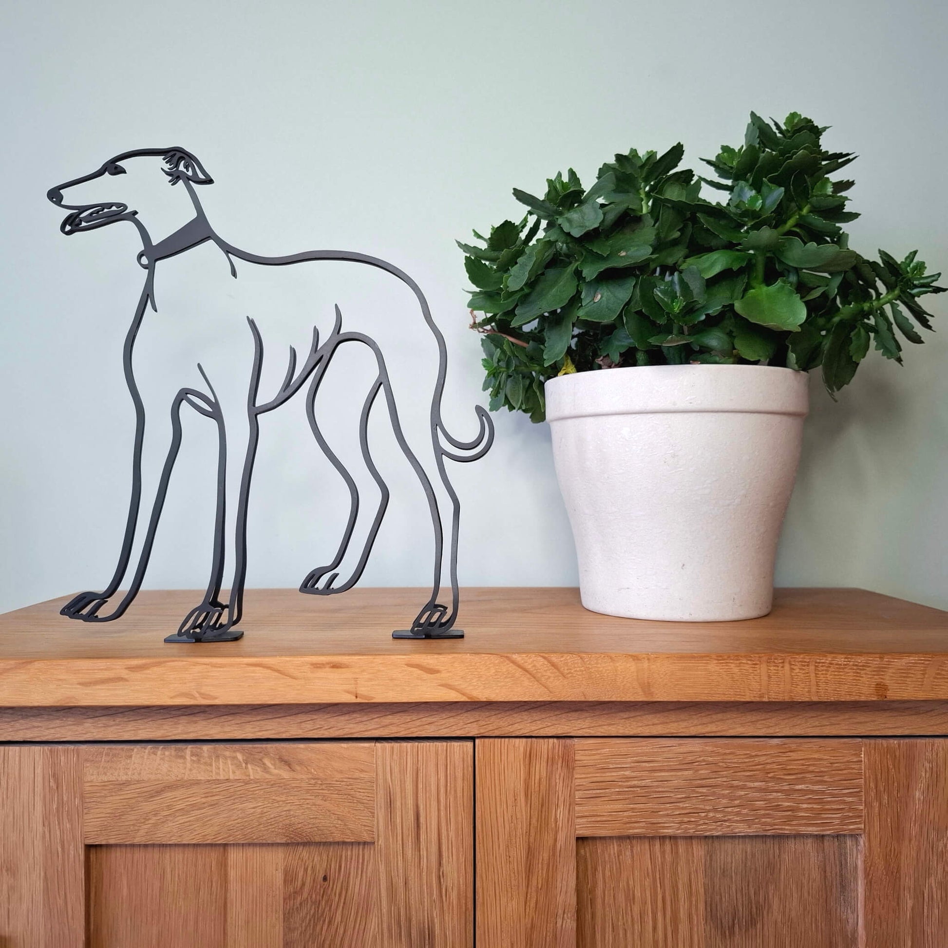 greyhound dog sculpture on a wooden surface next to a plant